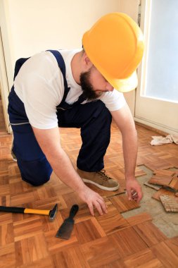 İnşaat işçisi ve inşaatçı daire yenileme üzerinde çalışıyor. Handyman sarı çekiç ve kazıma aracı kullanarak eski ahşap parke döşeme kaldırıyor. Oluşturucu parke zemin sökün.
