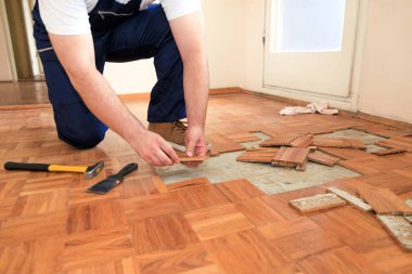 İnşaat işçisi ve inşaatçı daire yenileme üzerinde çalışıyor. Handyman sarı çekiç ve kazıma aracı kullanarak eski ahşap parke döşeme kaldırıyor. Oluşturucu parke zemin sökün.