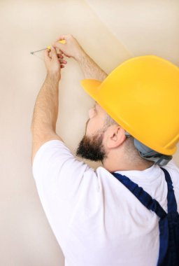 İnşaat işçisi ve tamirci daire yenileme çalışmaları. İnşaat sahasında duvardan çıkan sarı tornavida vidaları kullanan inşaatçı. Ev yenileme konsepti. İnşaat aleti.