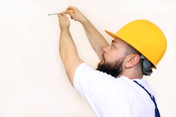 Construction worker and handyman works on renovation of apartment. Builder using yellow screwdriver screws steel screw out of wall on construction site. House renovation concept. Construction tool.