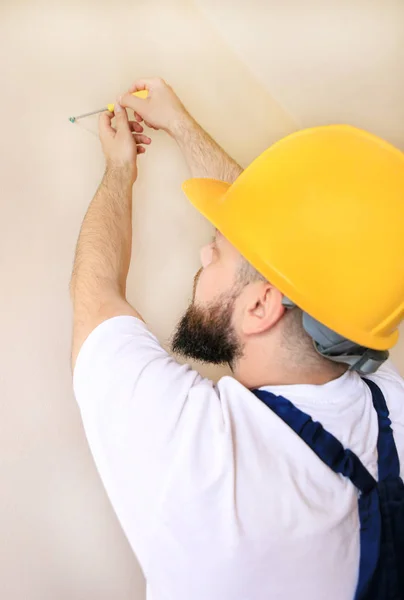 Construction worker and handyman works on renovation of apartment. Builder using yellow screwdriver screws steel screw out of wall on construction site. House renovation concept. Construction tool.