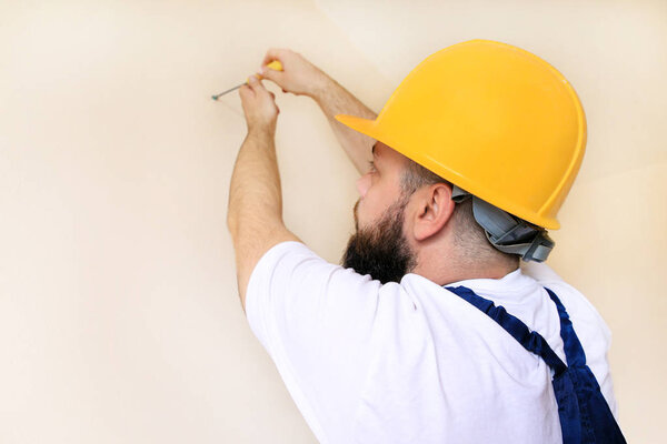 Construction worker and handyman works on renovation of apartment. Builder using yellow screwdriver screws steel screw out of wall on construction site. House renovation concept. Construction tool.