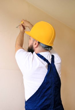 İnşaat işçisi ve tamirci daire yenileme çalışmaları. İnşaat sahasında duvardan çıkan sarı tornavida vidaları kullanan inşaatçı. Ev yenileme konsepti. İnşaat aleti.
