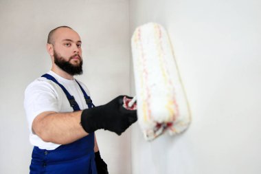 İnşaat işçisi dairede tadilat yapıyor. İnşaat alanındaki beton duvar odasının beyaz boya fırçasıyla boyanmış profesyonel bir boyacı. Ev yenileme konsepti.