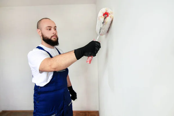 Bouwvakker doet afwerking renovatie in het appartement. Professionele schilder aannemer met behulp van witte verf roller borstel schilderen van beton muur kamer op de bouwplaats. Huisrenovatieconcept. — Stockfoto