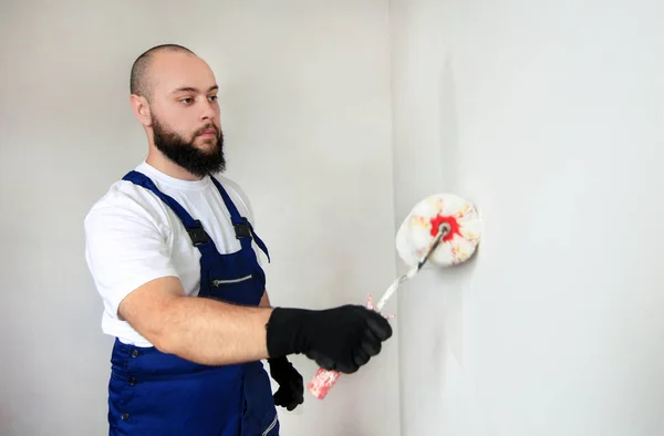 Építési munkás csinál befejezni felújítás lakásban. Professzionális festő vállalkozó segítségével fehér festék görgő ecset festés beton fali helyiség az építési területen. Lakásfelújítási koncepció. — Stock Fotó