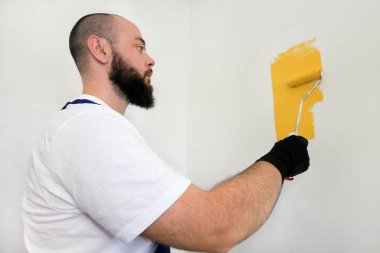 İnşaat işçisi ve tamirci dairede tadilat yapıyor. Profesyonel ressam, inşaat alanında sarı renkli duvar fırçası boyası kullanıyor. Ev yenileme konsepti.