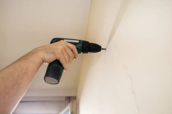 Construction worker and handyman works on renovation of apartment. Builder using electric screwdriver and screwing screw out of wall on construction site. Home renovation concept. Construction tool.
