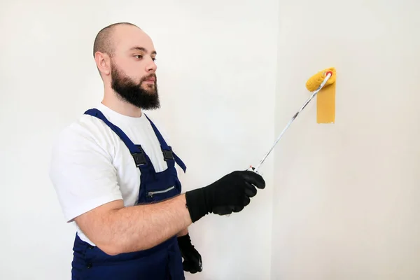 Építőmunkás és ezermester befejezi a felújítást a lakásban. Professzionális festő segítségével festék görgő ecset festmény fal sárga színű építési területen. Lakásfelújítási koncepció. — Stock Fotó