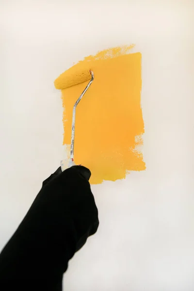 Construction worker and handyman doing finish renovation at apartment. Professional painter using paint roller brush painting of wall with yellow color on construction site. Home renovation concept. — Stock Photo, Image