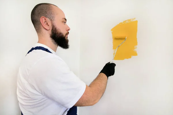 Bouwvakker en klusjesman doen renovatie in appartement. Professionele schilder met behulp van verf roller borstel schilderen van de muur met gele kleur op de bouwplaats. Huisrenovatieconcept. — Stockfoto
