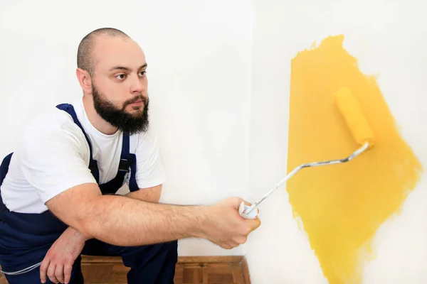 Bouwvakker en klusjesman doen renovatie in appartement. Professionele schilder met behulp van verf roller borstel schilderen van de muur met gele kleur op de bouwplaats. Huisrenovatieconcept. — Stockfoto