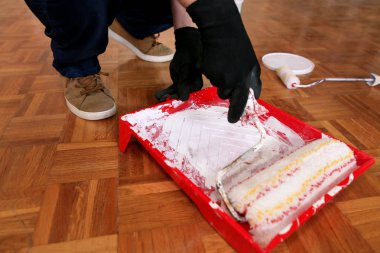 İnşaat işçisi ve tamirci dairede tadilat yapıyor. Eldivenli profesyonel ressam elinde beyaz tekerlekli fırça tutuyor ve boya ile kırmızı kaseyi karıştırıyor..