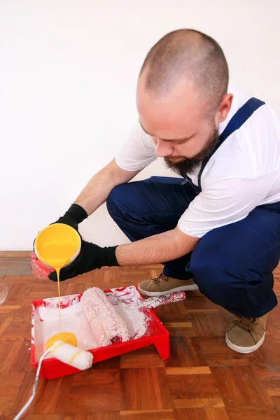 İnşaat işçisi ve tamirci dairede tadilat yapıyor. Siyah eldivenli profesyonel ressam boya karıştırmak için kovadan kırmızı kaseye sarı renk döker. Ev yenileme konsepti. — Stok fotoğraf