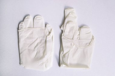 Beyaz arka planda bir çift tıbbi beyaz lateks koruyucu eldiven. Virüs, grip, koronavirüs (COVID-19) ve bakteri bulaşmasına karşı koruyucu tek kullanımlık eldivenler. Sağlık ve Cerrahi Konsept.