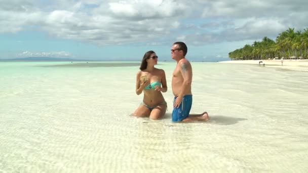 A man and a woman with a smartphone are sitting in the sea offshore — Stock Video