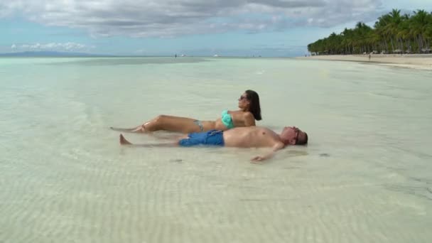 Жінка в купальнику і чоловік в шортах лежить на морі біля берега і засмагає — стокове відео