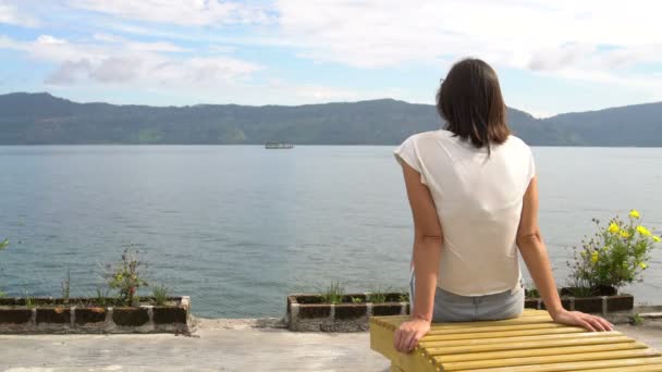 Una mujer se sienta junto al río con vistas a las montañas — Vídeos de Stock