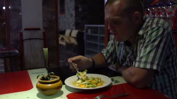 Un hombre está comiendo verduras guisadas en un café sentado a la mesa. — Vídeos de Stock