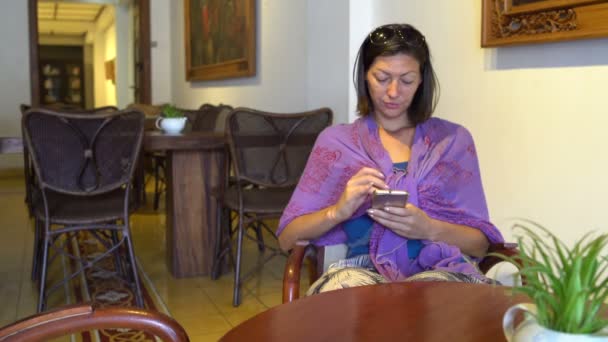 Eine Frau sitzt in der Cafeteria am Tisch und benutzt ein Smartphone — Stockvideo