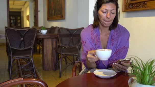 Mujer sentada a la mesa en la cafetería bebiendo café y usando smartphone — Vídeos de Stock