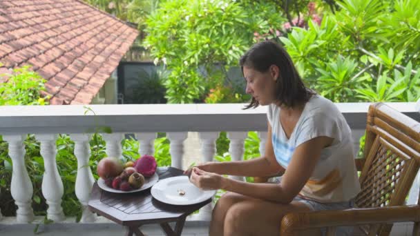Женщина, сидящая на балконе, очищает салаккские фрукты и ест — стоковое видео