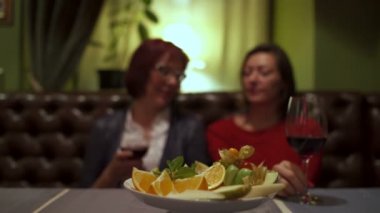 Restoran konuşurken bir masada oturan iki kadın gözlük tıklatması ve kırmızı şarap içmek.