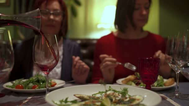 Les gens s'assoient au restaurant. Le serveur verse le vin d'une carafe dans un verre — Video