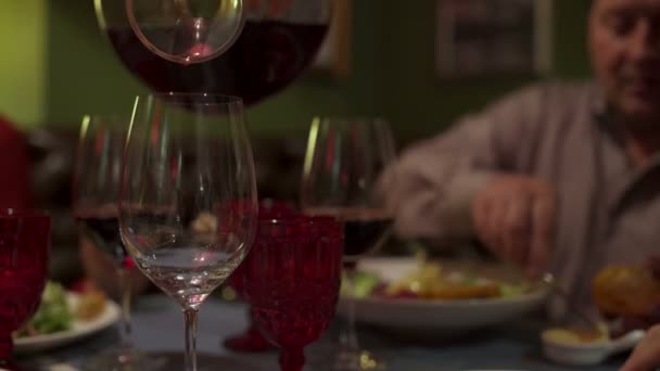 De ober giet de wijn in het glas van karaf wijn. Mensen eten zitten aan de tafel — Stockvideo