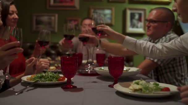 Le persone si siedono a un tavolo nel ristorante battono i bicchieri e bevono vino rosso — Video Stock