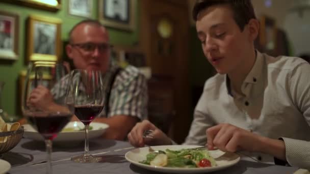 Человек ест и разговаривает с подростком за столом в ресторане — стоковое видео