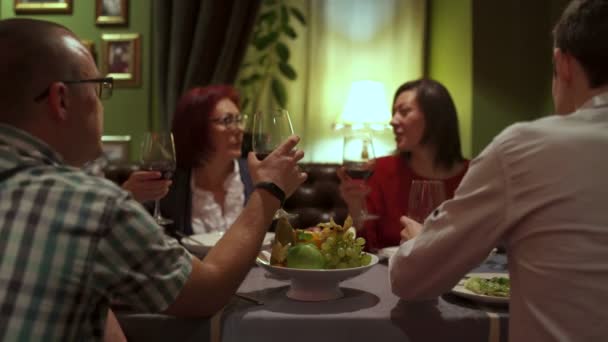 Amigos sentados em uma mesa no restaurante levantou copos com vinho tinto — Vídeo de Stock