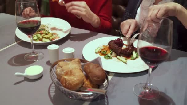 Twee vrouwen zitten aan een tafel in het restaurant en eten salade en rundvlees biefstuk. — Stockvideo