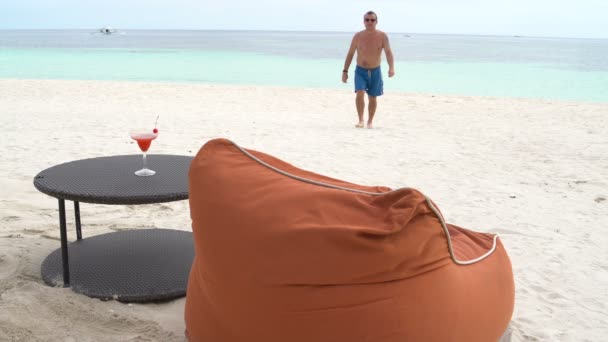 Um homem se deita em uma cadeira de praia e bebe coquetel — Vídeo de Stock