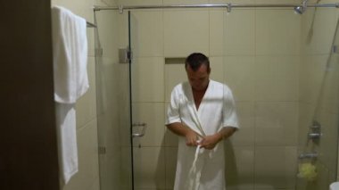 Bir adam bir bornoz giyiyor ve duştan geliyor