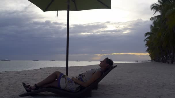 Een vrouw ligt op een chaise lounge aan zee bij zonsondergang — Stockvideo