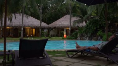 Akşam Açık Yüzme Havuzu. Bir adam bir güneşlenme yatıyor