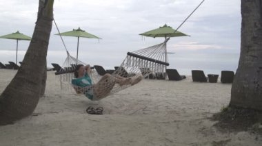 Kadın akşam deniz kıyısında bir hamakta yatıyor