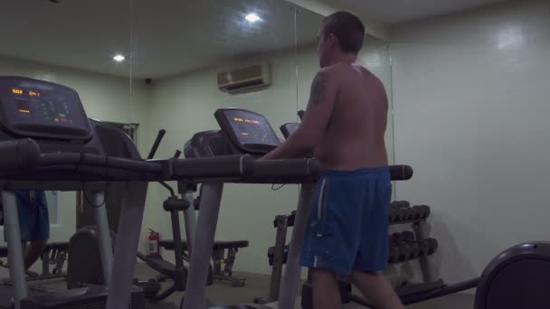 Un homme au gymnase sur le tapis roulant traite — Video