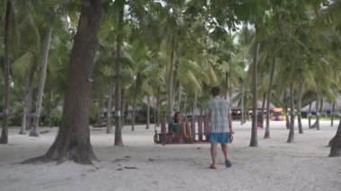 Avuç içi arasında bir salıncak üzerinde oturan bir bayan. Bir adam gelir ve kadının yanında oturur