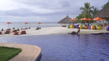 Kadın denizin kenarında açık havuzun yanında oturan bir mayo