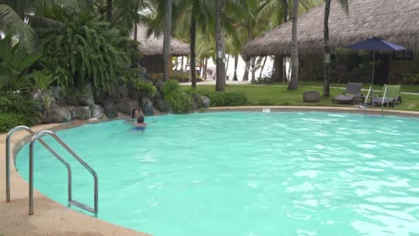 Una mujer en la piscina está debajo de una cascada. El hombre nada hasta la mujer y la besa . — Vídeo de stock