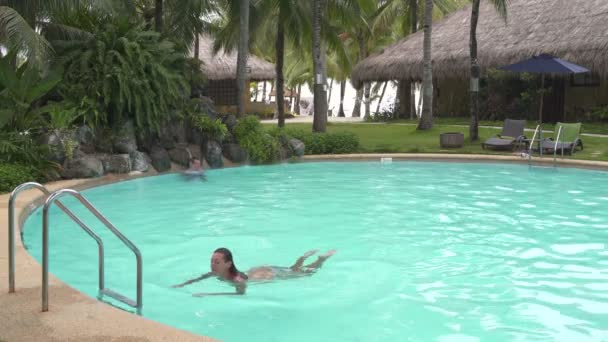 Adam bir havuzda bir yapay şelale altında duruyor. Merdivenlerden yukarı ve dışarı havuzun kadın yüzüyor — Stok video