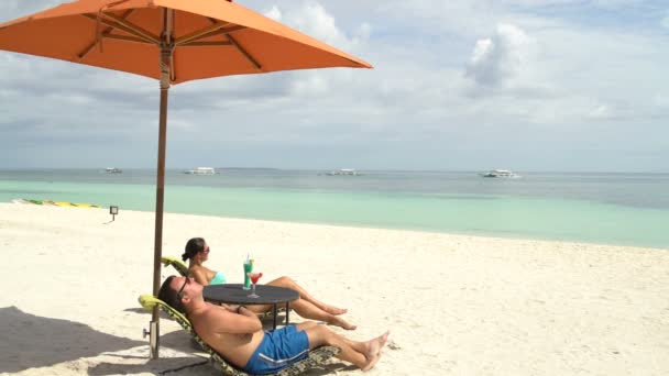 Un hombre y una mujer tomando el sol en las tumbonas en el mar — Vídeos de Stock