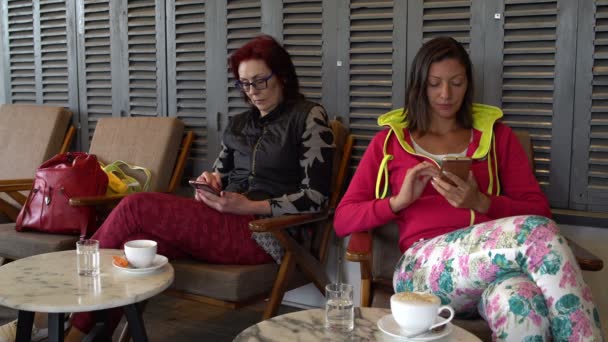 Mulheres em um café com smartphones. A menina coloca o telefone na mesa e bebe café — Vídeo de Stock