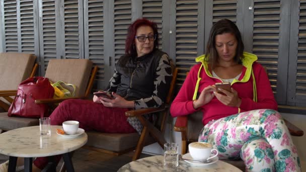 Mulheres sentam-se em um café com Smartphones e conversam — Vídeo de Stock