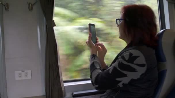 Uma mulher está tirando fotos em um smartphone da janela do trem — Vídeo de Stock