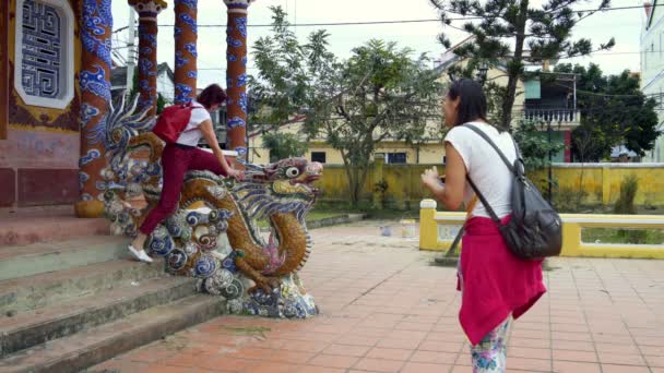 A girl is taking pictures of a woman sitting on a dragon statue — Stock Video