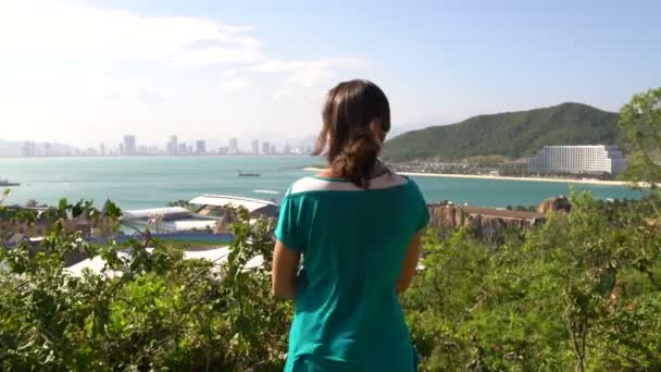 Uma mulher olha de uma altura para o mar e montanhas — Vídeo de Stock