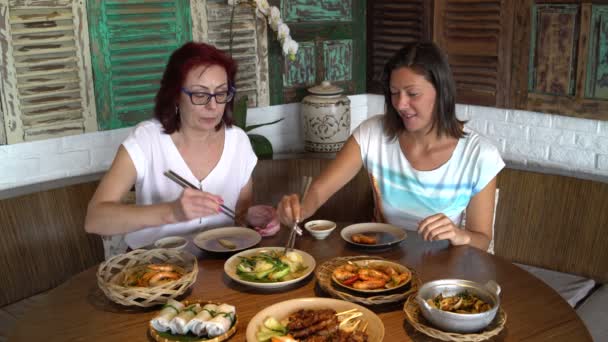 Frauen sitzen an einem Tisch mit verschiedenen Gerichten und stellen sich in eine Schüssel mit Essstäbchen — Stockvideo